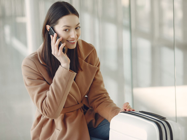 Traveler talking on a phone beside a suitcase at an airport.