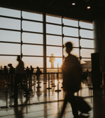 Travelers silhouetted against terminal windows in warm sunlight.